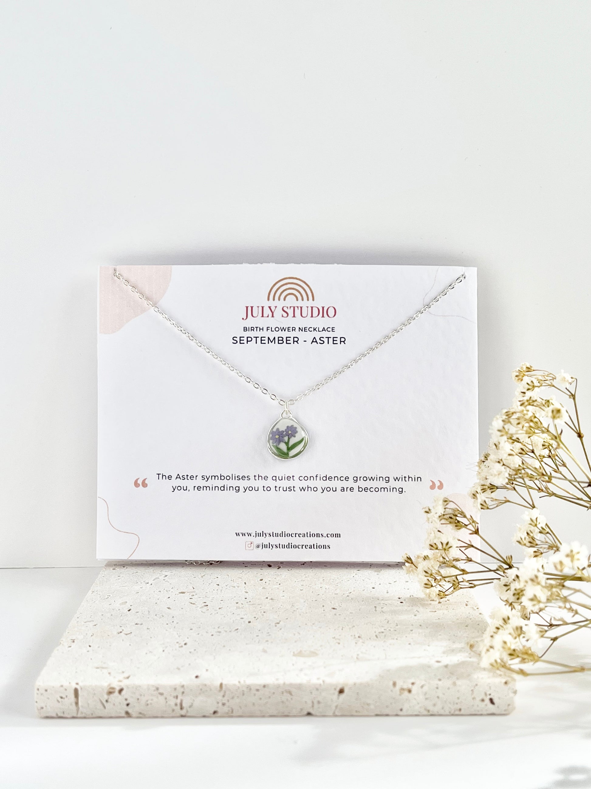 Silver clay necklace with a floral pendant on a white card with 'July Studio' branding, placed on a light surface with dried flowers.