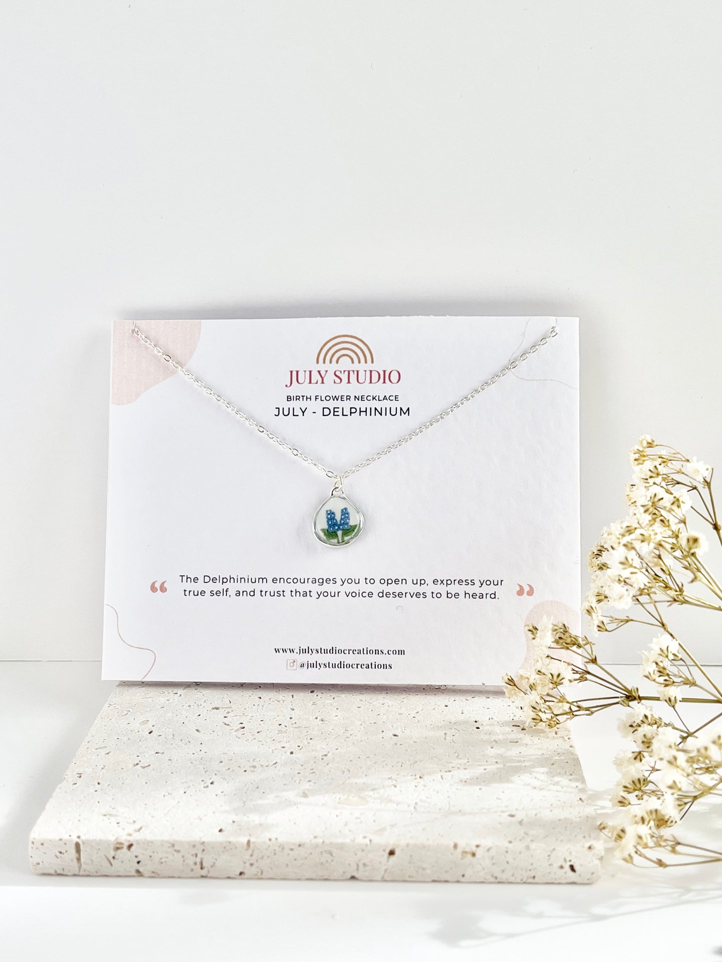 Silver clay necklace with floral pendant on a jewellery card, placed on a white surface with dried flowers.