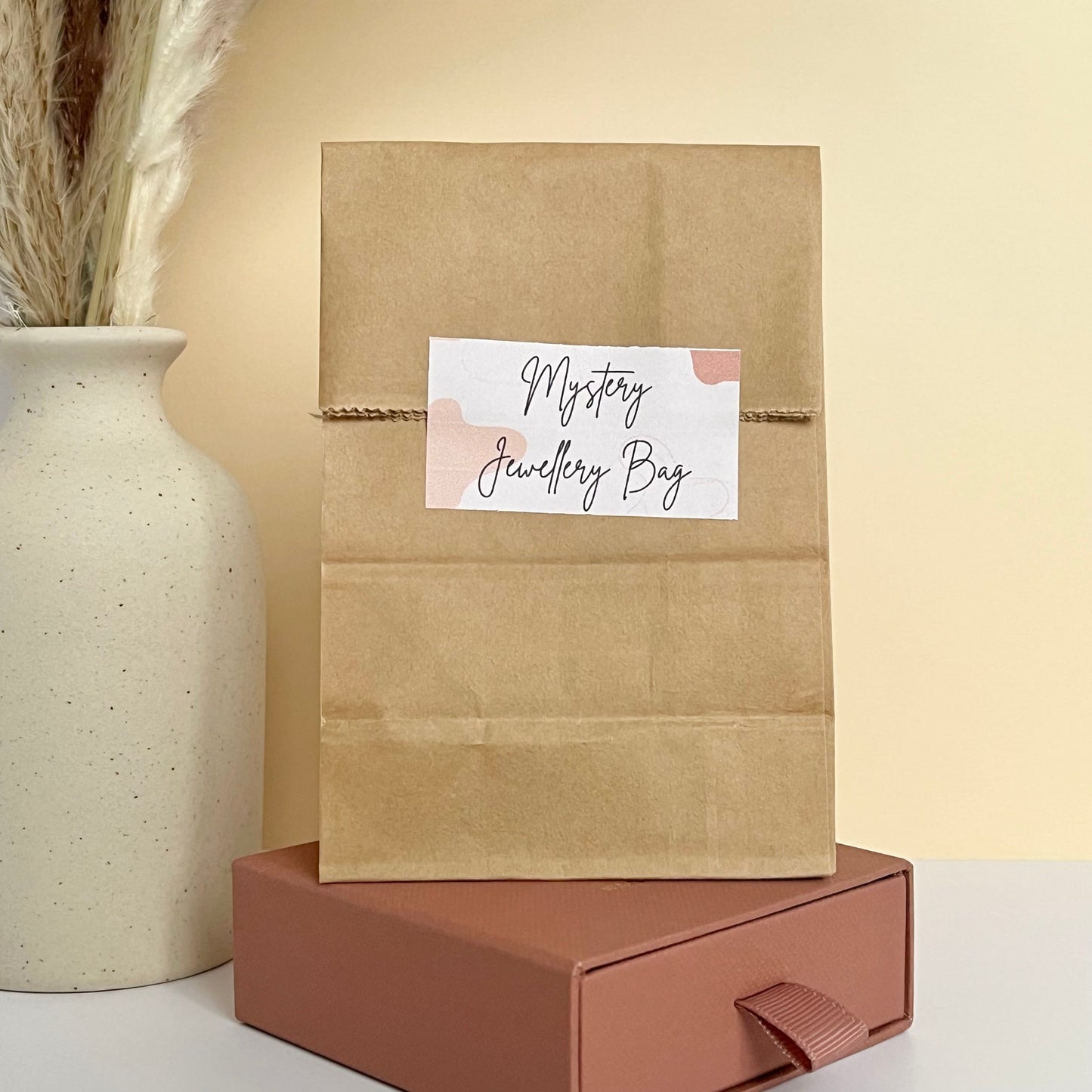 A brown craft bag with a polymer clay jewellery mystery bag sticker against a beige background