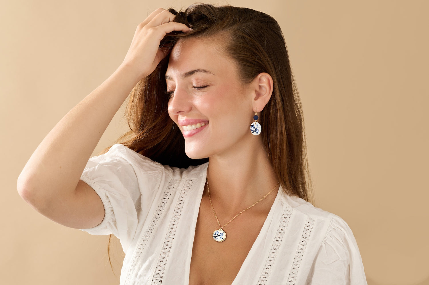 Smiling woman wearing an arch earrings with a blue and white floral pattern against a white background.