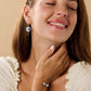 Woman wearing blue and white china floral jewellery set with dangle earrings and dainty bracelet against beige background