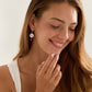 Smiling woman wearing a cherry blossom dainty clay bracelet and cherry blossom clay dangle earrings with a white background